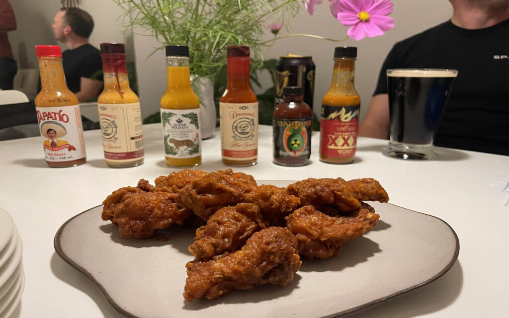 Crispy hot wings on a plate and the lineup of our hot sauces behind.